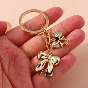 Elegant gold bow keychain with pearl and rhinestone accents held against pink background
