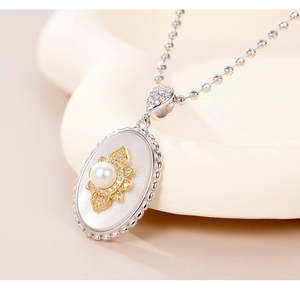 Close-up of oval pendant necklace featuring white pearl, gold floral motif and shell inlay