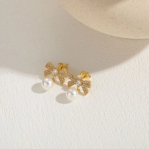 Detail of gold bow earrings with pavé zircon stones and dangling white round pearls