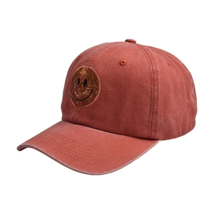 Detailed view of brick red washed baseball cap featuring a golden sequin smiley face patch