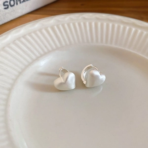 Macro shot of matte silver heart-shaped hoop earrings on a white ceramic tray