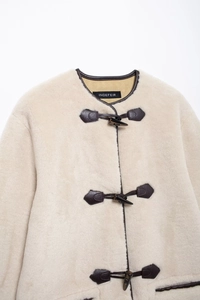 Dettaglio del cappotto in pelliccia con chiusura alamaro vintage e bordi in pelle marrone