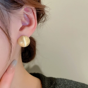 Close-up of elegant gold hemispherical stud earrings on model showing matte finish