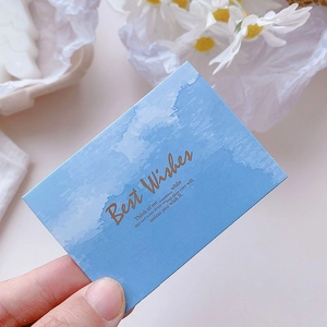 Blue minimalist greeting card with gold foil text and watercolor clouds held by hand
