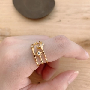 Detailed view of layered gold star and moon rings with zircon on a person's finger