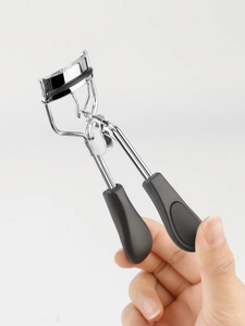 Detail of a portable stainless steel eyelash curler with a black anti-slip handle grip