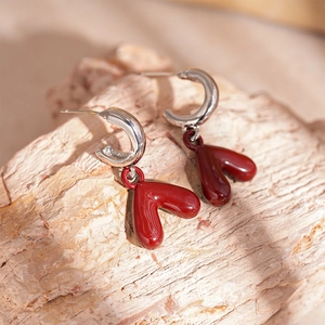 Macro shot of silver C-shape earrings with deep red heart pendants on natural rock