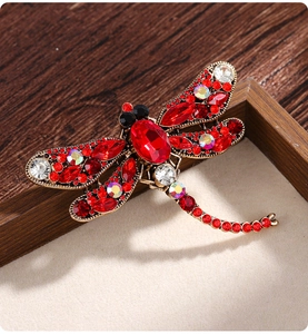Macro shot of vintage dragonfly brooch with red and white crystal inlays on wood