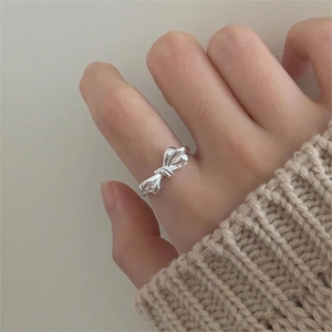 Detail of 925 sterling silver bow ring worn with a soft beige knitted sweater