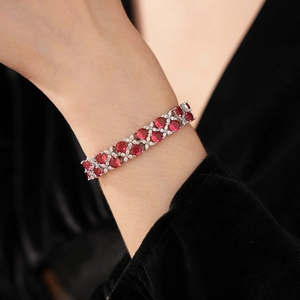 Detailaufnahme eines silbernen Blumenarmbands mit roten Zirkonia am weiblichen Handgelenk