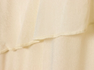 Close-up of light beige chiffon fabric showing delicate tiered layers and stitching detail