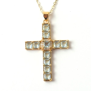 Macro shot of gold cross pendant with blue square gemstones and small white diamonds
