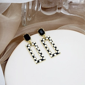 Detail of geometric drop earrings featuring black and white polka dots and gold frame