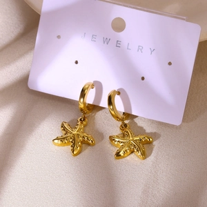 Gros plan de boucles d'oreilles étoile de mer dorées sur carte de bijoux blanche