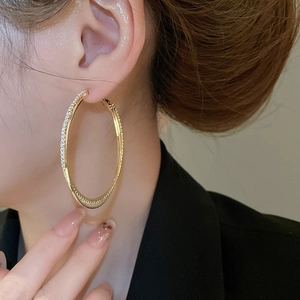 Detailed close-up of a model wearing gold intertwined double hoop earrings with pavé crystals