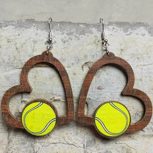 Detail von herzförmigen Holzohrringen mit Tennisballmuster auf steinerner Fläche