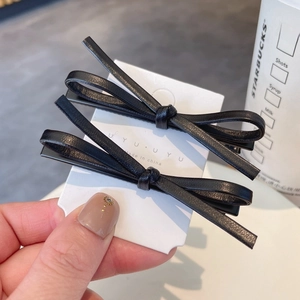 Set of two black leather bow hair clips in minimalist style on a display card