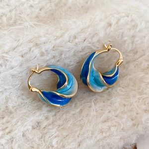 Close-up of twisted gold hoops with blue gradient enamel on soft beige fabric