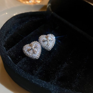 Macro shot of sparkling heart stud earrings with zircon inlay and cross detail