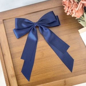 Detail of a large navy blue satin ribbon bow hair clip on a minimalist wooden tray