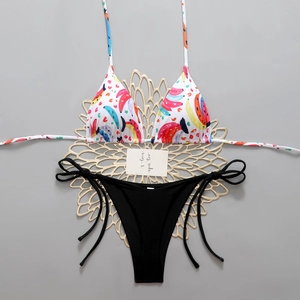 Detail of banana print halter bikini top and black side-tie bottom on gray surface