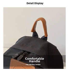 Close-up of black canvas backpack featuring brown leather handle and two-way zippers