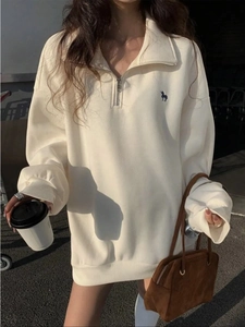 Λεπτομέρεια του κεντήματος μονόκερου στο oversized λευκό φούτερ με φερμουάρ στο κολάρο