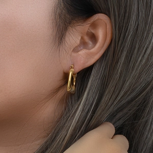 Close-up of golden geometric triangle earrings with textured wire wrap on a model