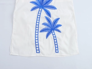 Detailed close-up of blue palm tree embroidery on a white vacation style skirt