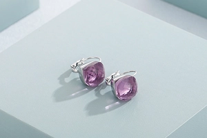 Detailed close-up of lavender cushion-cut crystal earrings on a blue geometric base