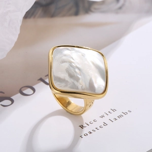 Detailed view of square shell inlay on a golden stainless steel ring on book