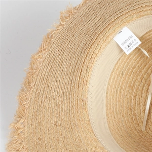 Detail showing 100% natural raffia straw texture and handmade frayed fringe edges on the hat
