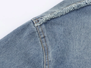 Detail of light blue denim jacket with contrast stitching and distressed raw hem edge
