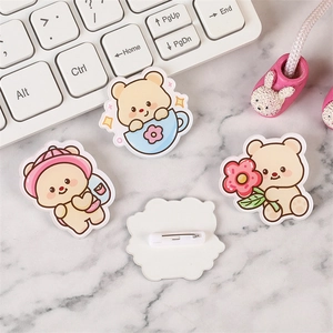 Cute yellow acrylic bear brooches and pink flower badges on a desk setup with keyboard