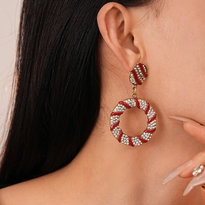 Detail view of model wearing gold earrings with red enamel stripes and white diamonds