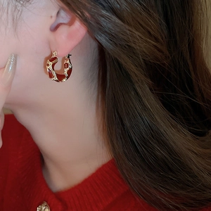 Close-up of model wearing U-shaped red enamel and gold earrings with vintage aesthetic