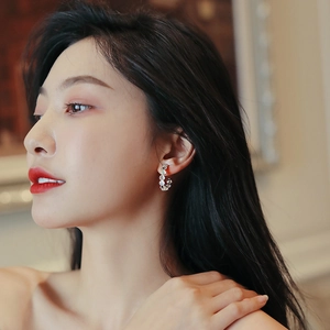 Macro shot of silver C-shaped hoop earrings with cat-eye stones on model's ear