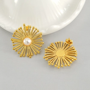 Minimalist golden sunburst stud earrings with central pearl on a ceramic plate
