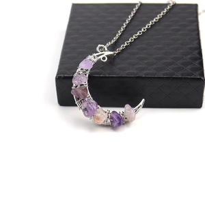 Detailed shot of silver crescent moon pendant with purple crushed crystal on a black gift box