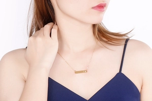 Close-up of golden horizontal bar necklace with heart engraving and zircon on neck