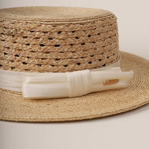 Handwoven raffia boater hat with a cream grosgrain ribbon and golden metal tag detail