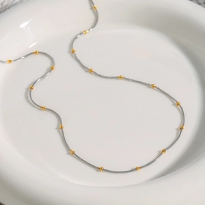 Detailed close-up of a silver minimalist chain necklace with gold beaded accents