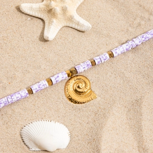 Détail d'un collier bohème en argile violette avec pendentif coquillage doré sur sable