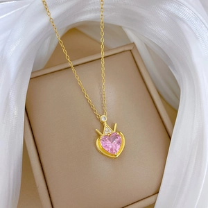 Detail of gold heart necklace with pink gemstone and crown pendant on silk fabric