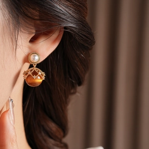 Close-up of a gold earring with tiger eye stone and crystal hollow cage on model