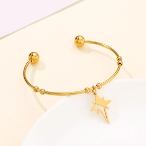 Close-up of golden stainless steel open bangle with hollow star charm on a white ceramic plate