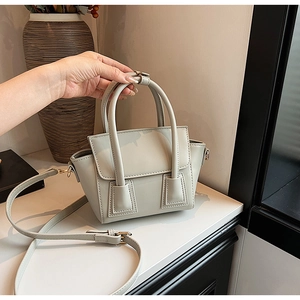 Detail of a beige structured trapezoid handbag with top handle and adjustable strap