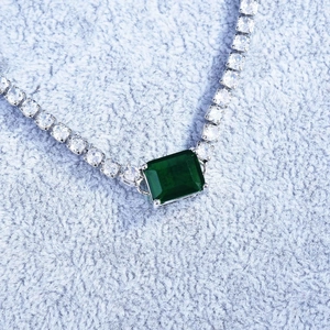 Macro view of luxury square-cut emerald necklace with pavé diamond halo set in silver