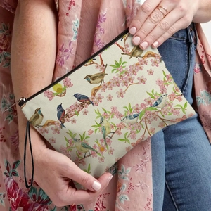 Floral makeup bag with bird prints and wristlet strap shown in casual hand-held use