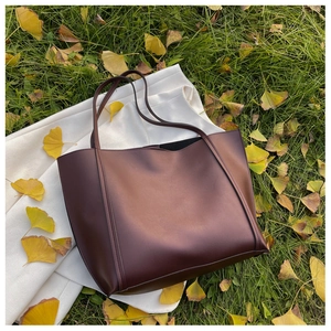Detail of a large brown leather tote bag on white blazer with autumn ginkgo leaves